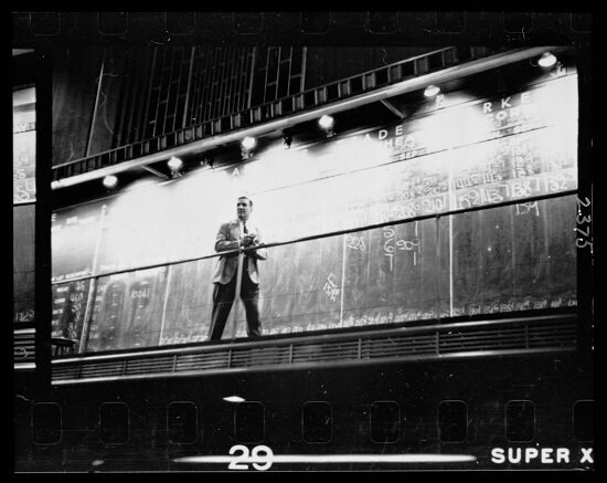 Unidentified man standing in front of a "Trade" board on which he records a "Market Score" at the Chicago Board of Trade