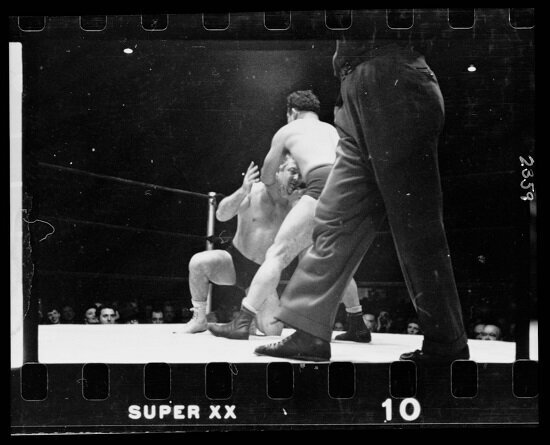 A wrestler holding Gorgeous George by the chin and back of the head, executing a maneuver during a wrestling match