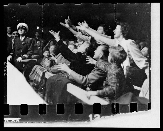 Several women at ringside, standing and reaching as if to catch something thrown by wrestler Gorgeous George who, though not visible in this image, was standing in the ring