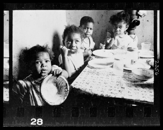 African American children seated around a table in an apartment, eating