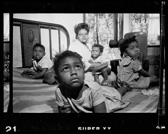 An African American woman and several children sitting on a bed in an apartment